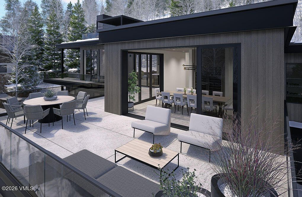 This image showcases a modern home's outdoor living space, featuring a spacious patio with a dining area and lounge seating. The patio is furnished with a round table, chairs, and comfortable lounge chairs, creating an inviting atmosphere for relaxation and entertainment. Large sliding glass doors seamlessly connect the indoor and outdoor spaces, enhancing the home's appeal for those seeking a luxurious and contemporary lifestyle.
