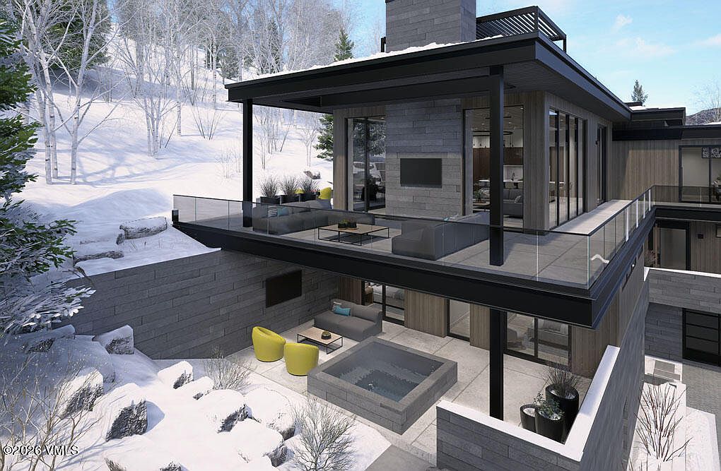 This image showcases a modern home's exterior, specifically highlighting the patio and balcony areas. The design features clean lines, with a combination of stone and wood finishes, and glass railings. A hot tub is visible on the lower patio, and comfortable seating arrangements are present on both levels, creating inviting outdoor living spaces.