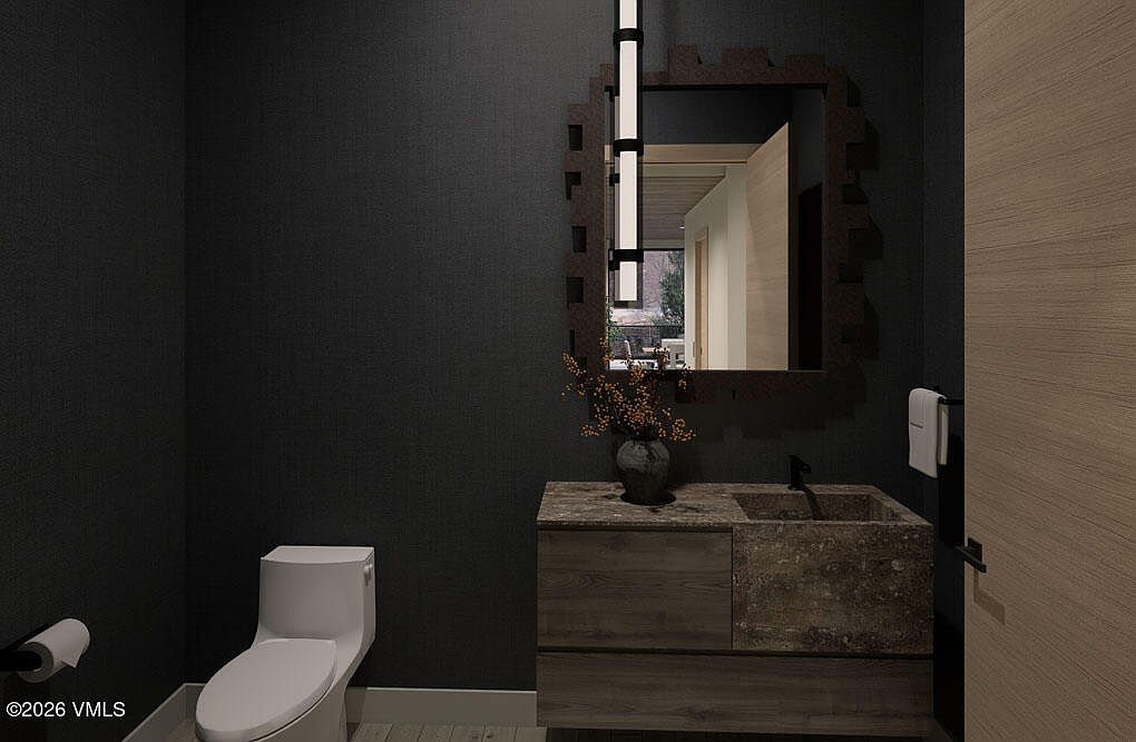 This is a modern guest bathroom featuring dark textured walls, a floating vanity with a stone countertop and integrated sink, and a contemporary mirror with integrated lighting. A white toilet sits to the left, and a light wood door is visible on the right. The overall aesthetic is sleek and sophisticated, creating a luxurious feel for guests.