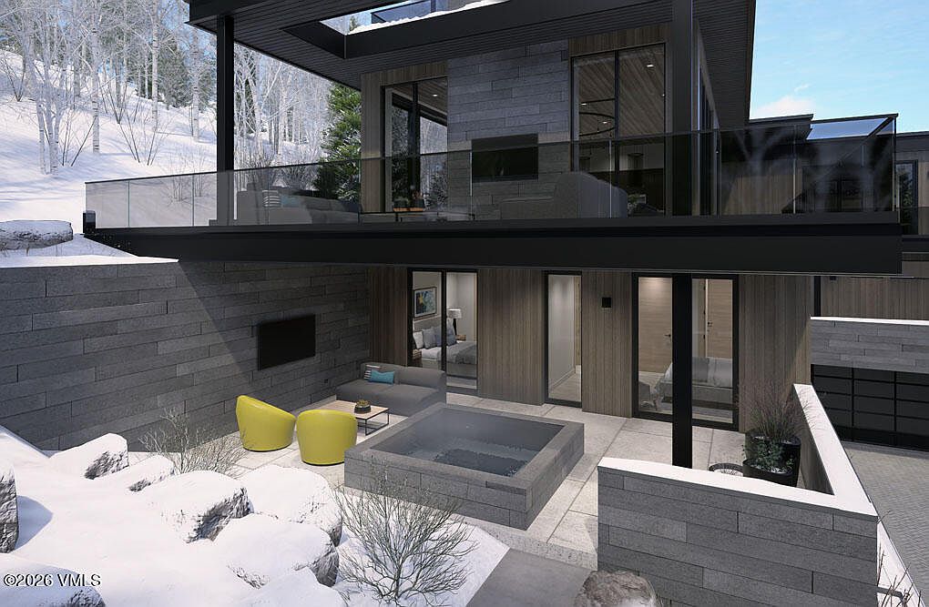 This image showcases a modern home's outdoor living space, featuring a patio with a sunken hot tub, contemporary furniture, and a built-in outdoor television. The design incorporates clean lines and natural materials, creating a luxurious and inviting atmosphere. The upper level has a balcony with glass railings, offering views of the surrounding snowy landscape.