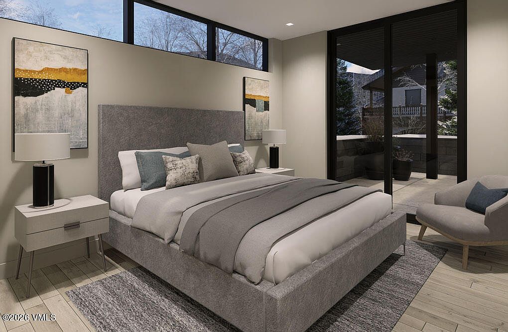 This is a primary bedroom featuring a gray upholstered bed with a matching headboard, complemented by neutral-toned bedding and pillows. The room is decorated with abstract artwork and modern bedside tables with lamps. A large sliding glass door leads to an outdoor space, enhancing the room's natural light and spacious feel.