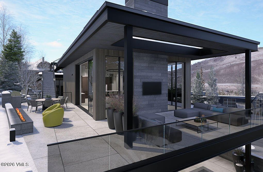 This image showcases a modern home's outdoor living space, featuring a spacious patio with a fire pit, comfortable seating, and a dining area. The design incorporates clean lines, a neutral color palette, and glass railings to maximize the mountain view. The space is designed for both relaxation and entertaining, blending seamlessly with the surrounding landscape.