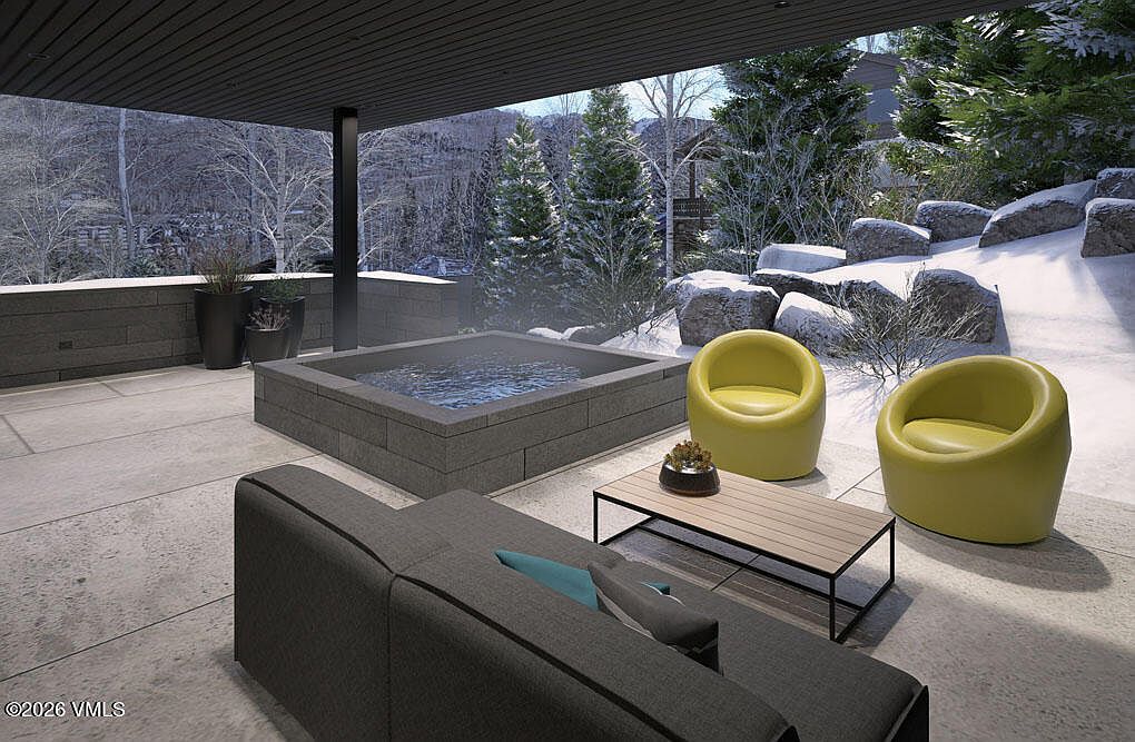 This image showcases a luxurious outdoor patio area, featuring a built-in hot tub, modern seating, and a sleek coffee table. The patio is surrounded by a snowy landscape with mature trees and rock features, creating a serene and private atmosphere. The design emphasizes relaxation and high-end outdoor living.