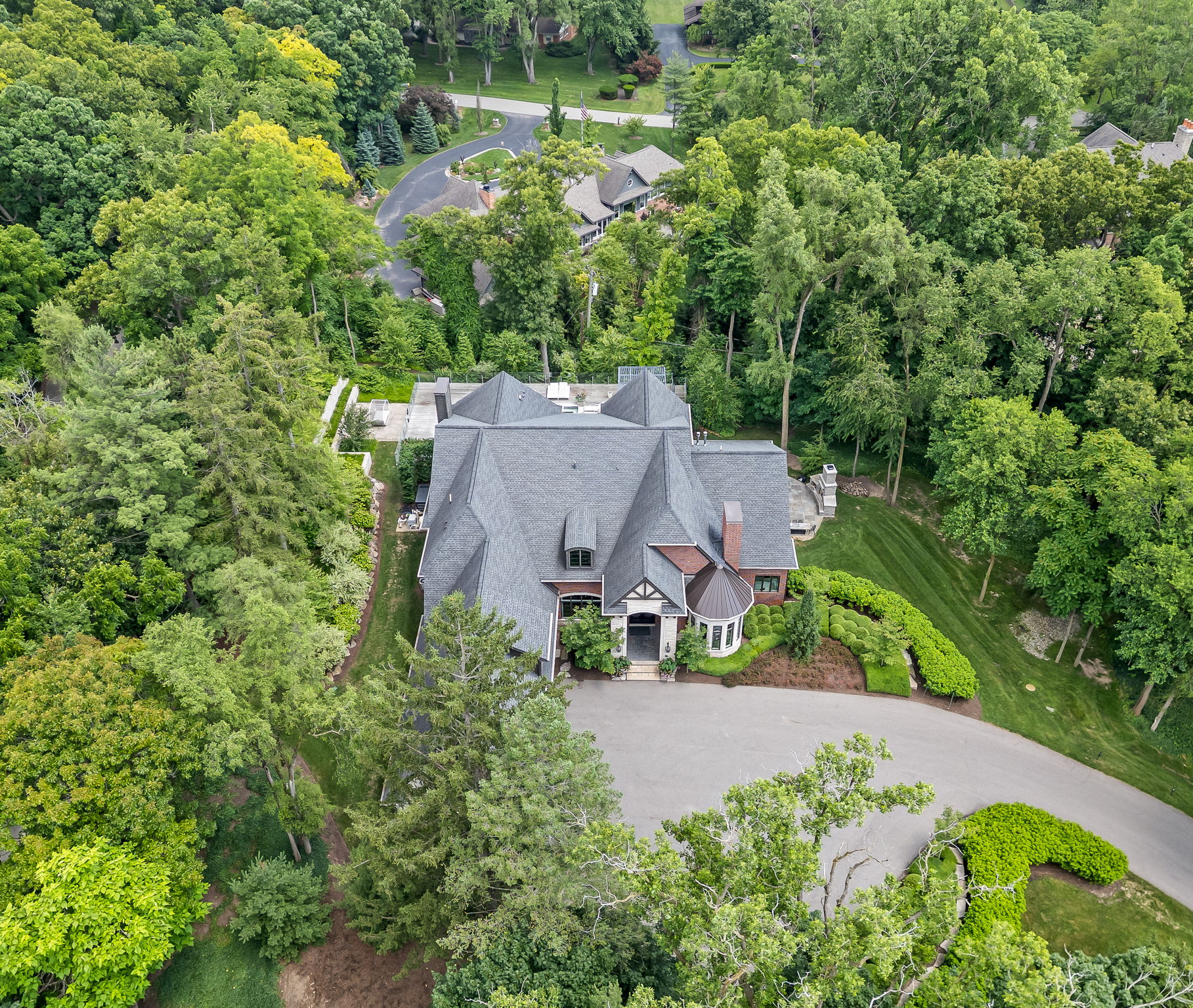 This aerial shot showcases a large, luxurious home nestled among lush greenery. The house features a complex roofline, a circular driveway, and meticulously landscaped grounds. The surrounding trees provide privacy and a sense of seclusion, creating an impressive estate.