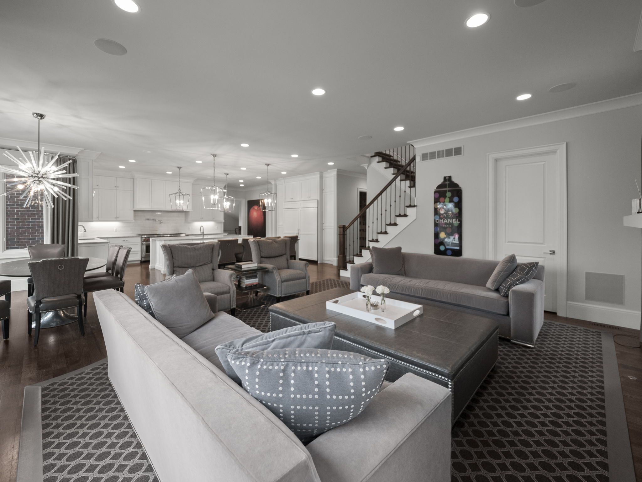 This is an interior shot of a living room that seamlessly blends into the kitchen and dining area. The living room features two large sofas, a dark-colored ottoman, and a patterned rug, creating a cozy yet sophisticated atmosphere. The open floor plan enhances the sense of space and connectivity, making it ideal for entertaining.