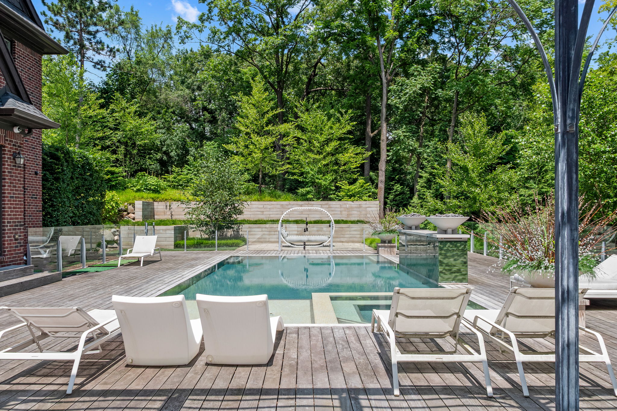 This image showcases a luxurious backyard pool area, complete with modern lounge chairs and a stylish circular daybed. The pool is surrounded by a wooden deck and lush greenery, creating a private and serene oasis. The design incorporates clean lines and high-end materials, suggesting a sophisticated and relaxing outdoor living space.