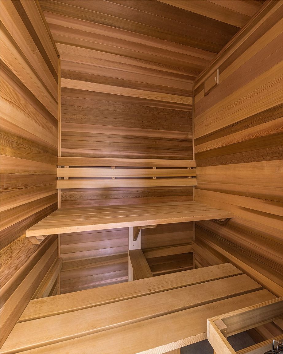 This is an interior shot of a sauna, featuring wooden walls and benches. The wood has a warm, natural tone, creating a relaxing and inviting atmosphere. The benches are arranged at different levels, providing ample seating space.