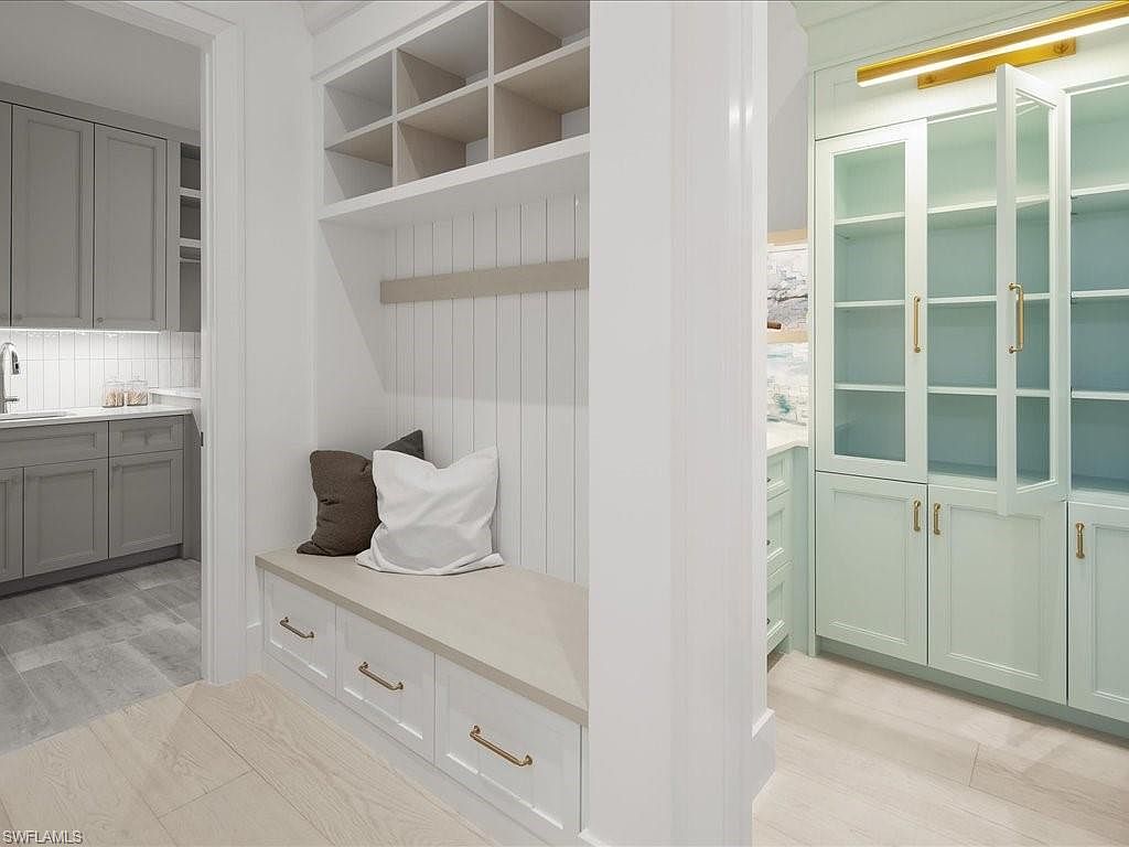 This interior shot showcases a well-organized laundry room or mudroom area. It features custom built-in cabinetry with open shelving, a bench seat with storage drawers, and a separate cabinet unit with glass doors, all in a light, neutral color palette. The design emphasizes functionality and storage, making it an appealing feature for potential homebuyers.
