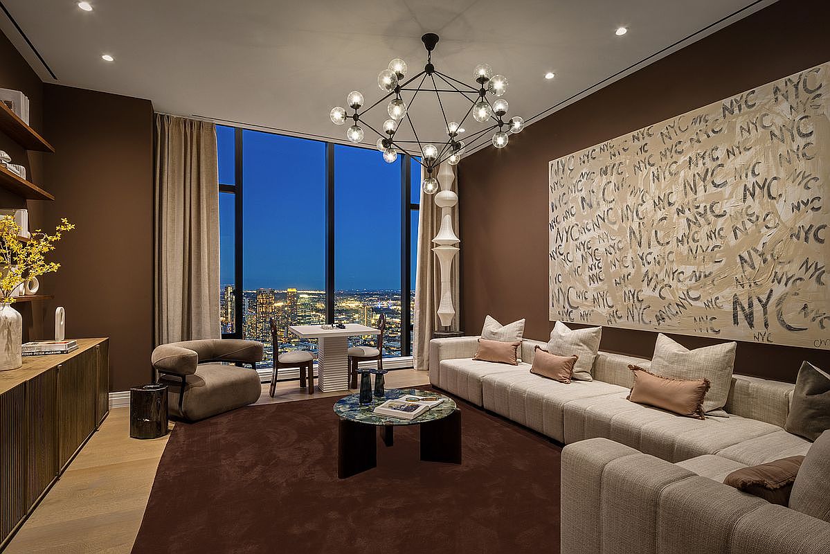 This sophisticated, modern living room features a striking floor-to-ceiling window offering a panoramic city skyline view at dusk. The space is anchored by a plush, dark brown area rug, a contemporary sofa adorned with neutral-toned pillows, and a unique circular marble coffee table. A large, artistic wall mural repeating the letters 'NYC' serves as a bold focal point, complemented by a dramatic, multi-bulb chandelier that adds a touch of luxury to the room.