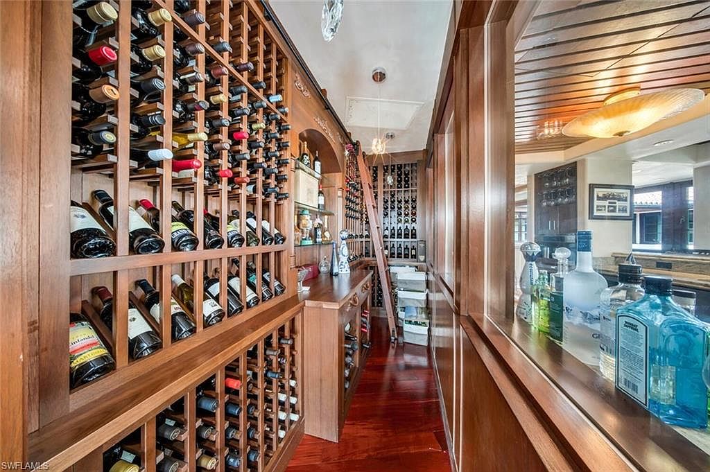 This is a well-stocked wine cellar featuring wooden racks filled with numerous bottles of wine. A rolling ladder provides access to the upper shelves, and a counter area offers space for preparation or display. The room has a warm, inviting ambiance with wood paneling and flooring, suggesting a sophisticated and curated space for wine enthusiasts.