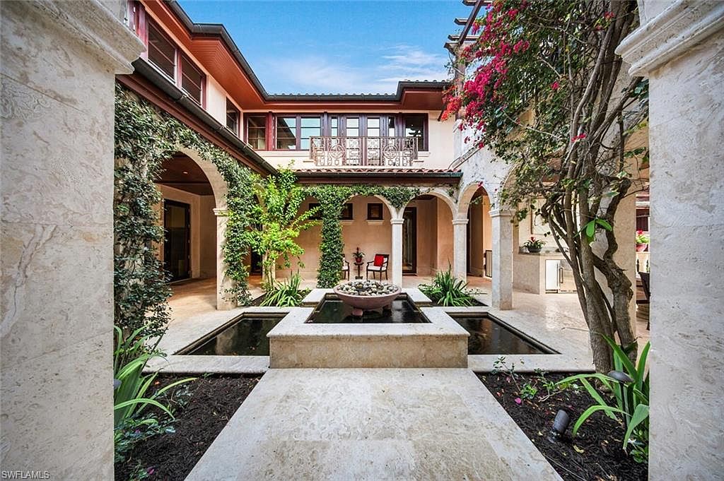 This image showcases a beautifully designed courtyard garden. A central water feature with a tiered fountain is surrounded by lush greenery and meticulously maintained landscaping. The architecture features arched walkways adorned with climbing vines, creating a serene and inviting outdoor space.