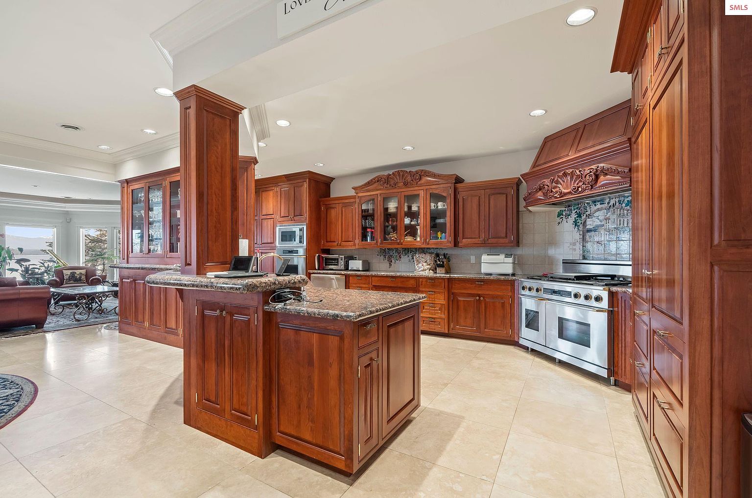This is a spacious kitchen featuring custom wood cabinetry, granite countertops, and stainless steel appliances. The kitchen island provides additional counter space and storage, while the ornate range hood adds a touch of elegance. The warm tones and ample lighting create an inviting atmosphere.