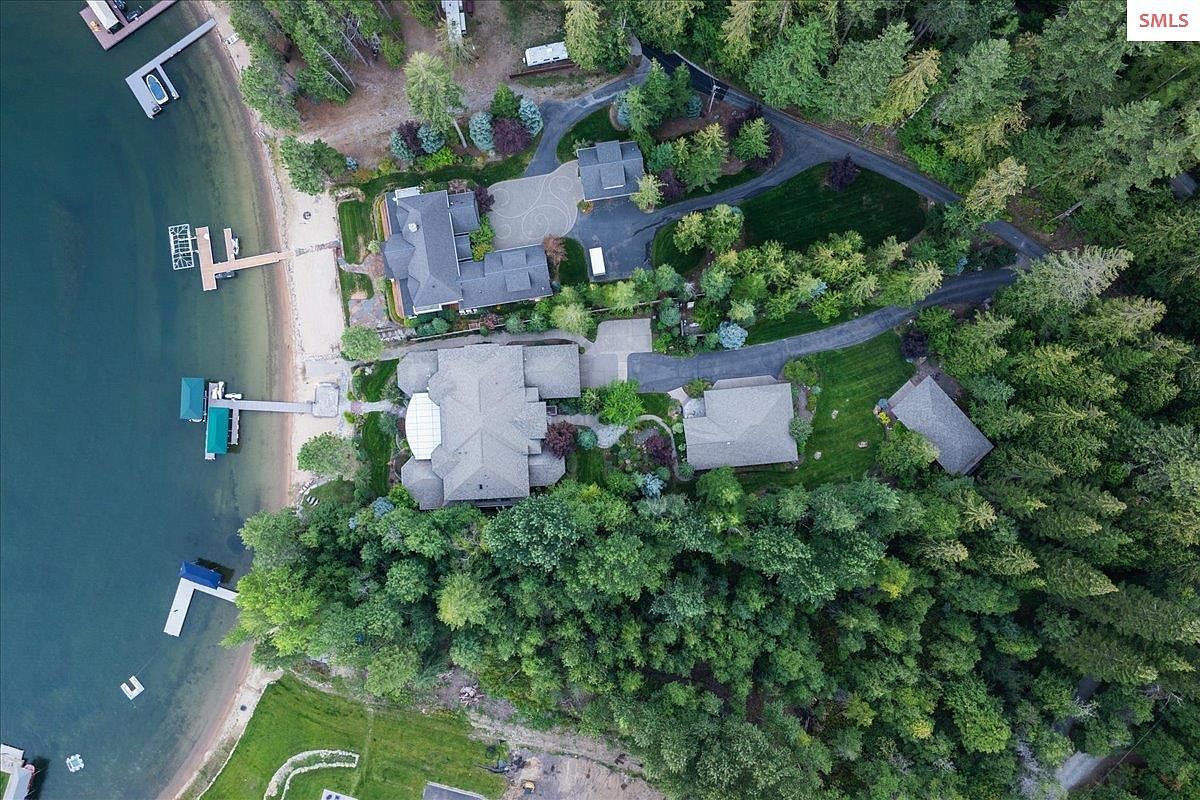 This aerial shot showcases a luxurious lakeside property featuring multiple houses with well-maintained lawns and mature trees. The houses have gray roofs and are connected by driveways. The lakefront includes docks and piers, enhancing the property's appeal for water activities.