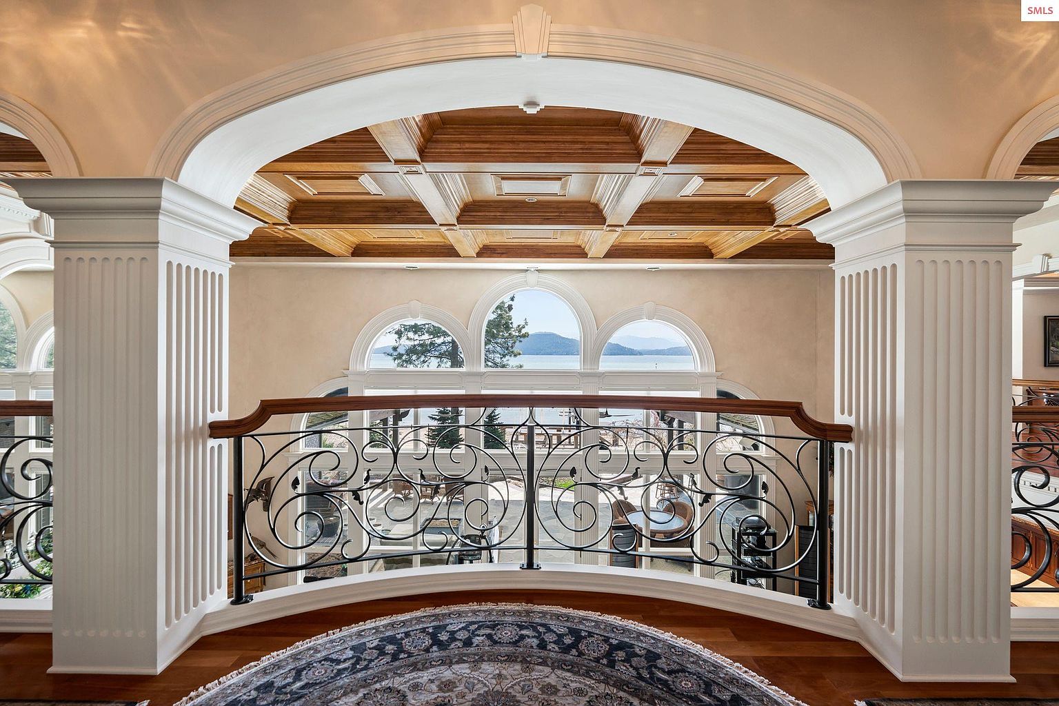 This interior shot showcases an elegant hallway or landing area with a decorative wrought iron railing and substantial architectural columns. The coffered ceiling adds a touch of sophistication, while arched windows provide natural light and a view of the water. The space is well-appointed and exudes a sense of luxury.
