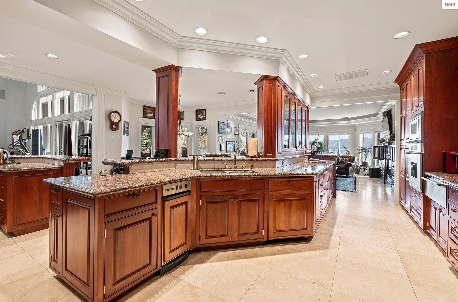 This is a spacious kitchen featuring custom wood cabinetry with granite countertops and tile flooring. The kitchen includes a large island with a sink and a breakfast bar, as well as built-in appliances. The space is well-lit with recessed lighting and natural light, creating a warm and inviting atmosphere.