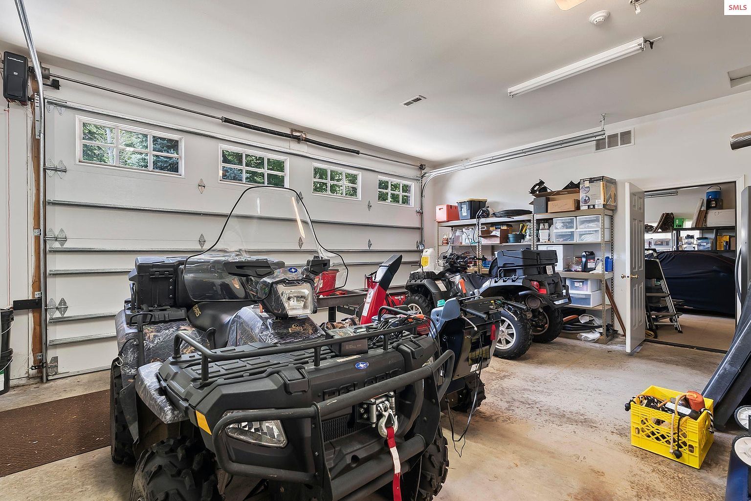 This is an interior shot of a garage featuring multiple ATVs. The garage has a white door with windows along the top and shelving units along the right wall. The floor is concrete and the overall impression is a well-organized and functional space.