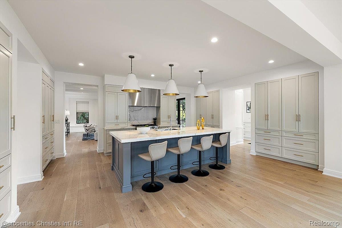This is a bright and spacious kitchen featuring a large center island with seating, pendant lighting, and custom cabinetry. The kitchen boasts modern appliances and a clean, elegant design. The hardwood flooring adds warmth to the space, creating an inviting atmosphere.