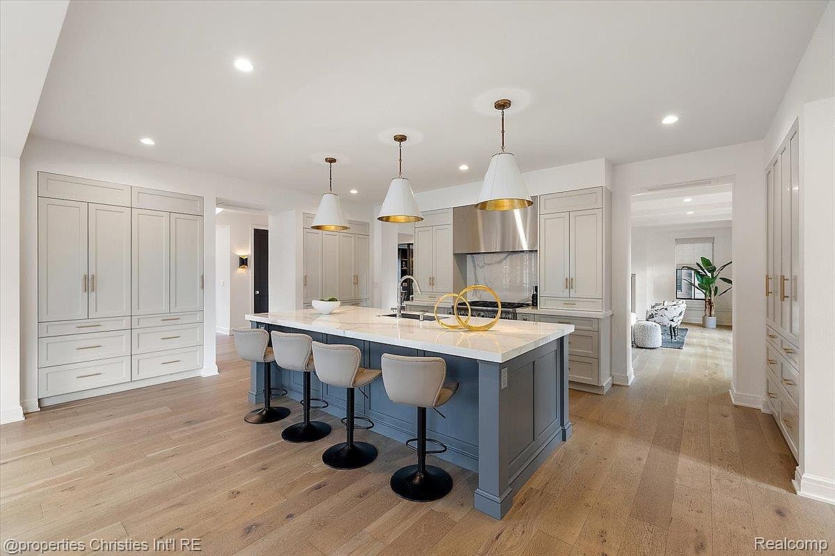 This is a bright and spacious kitchen featuring a large center island with seating, custom cabinetry, and modern pendant lighting. The kitchen is designed with a clean, contemporary aesthetic, and the hardwood flooring adds warmth to the space. The view is a wide shot from the side of the kitchen island.