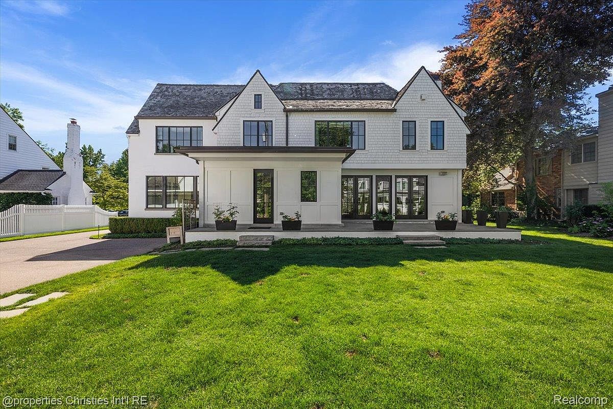This is a front exterior view of a two-story house with a well-manicured lawn. The house features a combination of white siding and dark-framed windows, with a covered porch area at the entrance. The overall impression is one of a stately and well-maintained property.