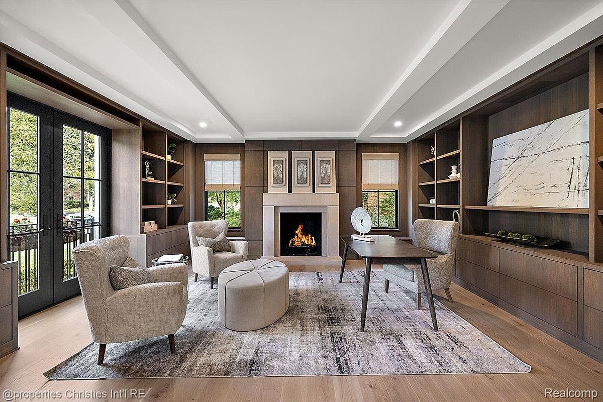 This is an interior shot of a sophisticated home office or study. The room features custom built-in shelving and cabinetry, a fireplace, and a neutral-toned rug that adds texture to the space. Natural light filters through the windows, creating a warm and inviting atmosphere, perfect for a productive workspace.