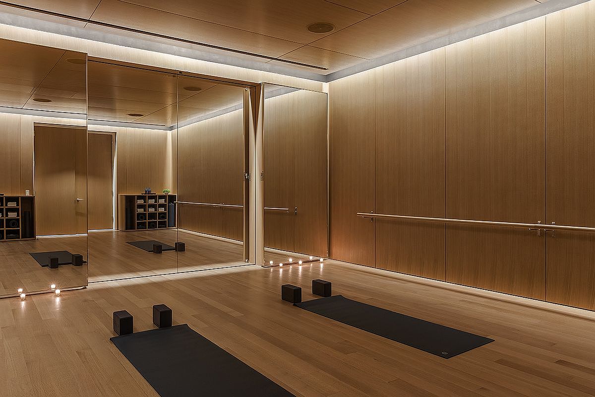 This serene home gym features warm wood-paneled walls and matching hardwood flooring, creating a cohesive and calming atmosphere. The space is equipped with yoga mats and blocks, with a ballet barre mounted along the wall and large mirrors that enhance the sense of depth. Soft, ambient lighting and small candles placed along the floor contribute to a tranquil, spa-like environment.