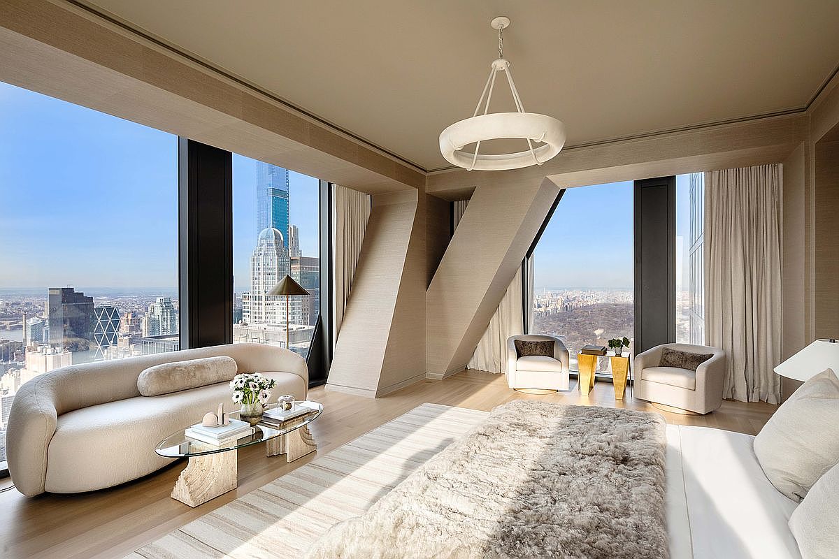 This luxurious primary bedroom features a sophisticated, neutral color palette and expansive floor-to-ceiling windows that offer panoramic city views. The room is furnished with a curved sofa, a glass-topped coffee table, and two plush armchairs, all arranged to maximize the natural light and scenery. A large, textured area rug anchors the space, while a modern, circular pendant light serves as a striking focal point above the bed area.