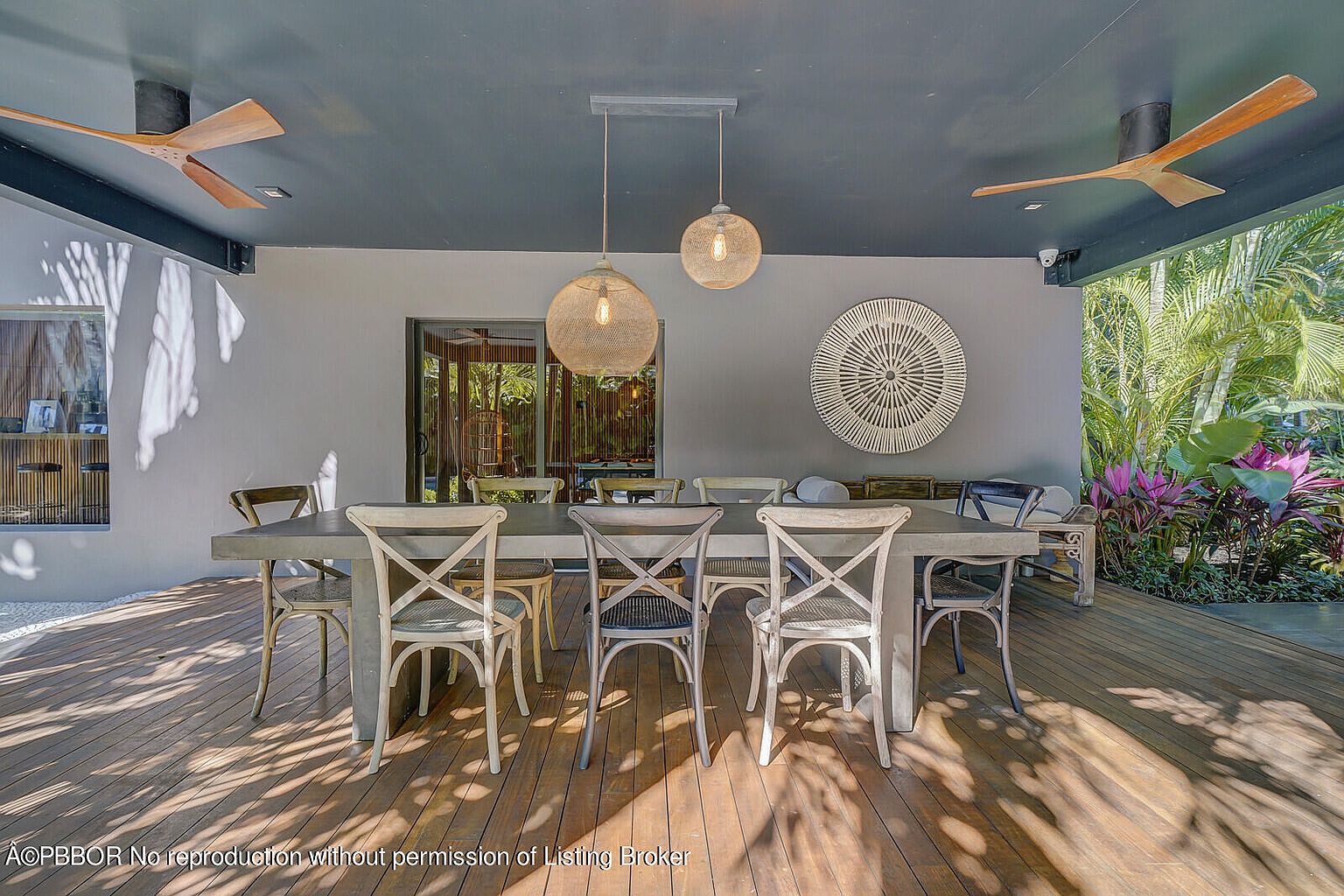 This image showcases a stylish outdoor dining area on a patio or deck. A large dining table with multiple chairs is the focal point, illuminated by pendant lights hanging from the ceiling. The space is open to a lush garden, creating a serene and inviting atmosphere perfect for entertaining or relaxing.