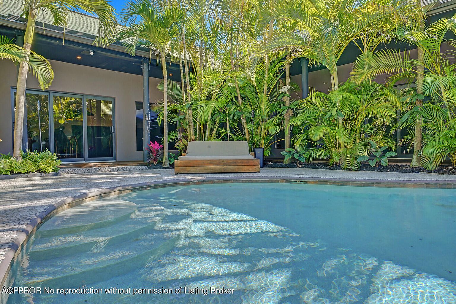 This image showcases a luxurious pool area, surrounded by lush tropical landscaping. The pool features steps leading into the water, and a modern outdoor lounge area is nestled among the palm trees. The overall impression is one of tranquility and upscale outdoor living.