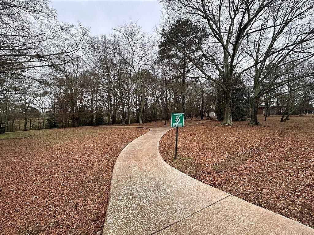 This image showcases a serene park pathway covered in fallen leaves, winding through a wooded area. A sign indicates the "Walford Trail Only" with a symbol prohibiting "Exercises of any kind". The scene evokes a sense of tranquility and natural beauty, highlighting the park's appeal as a recreational space.