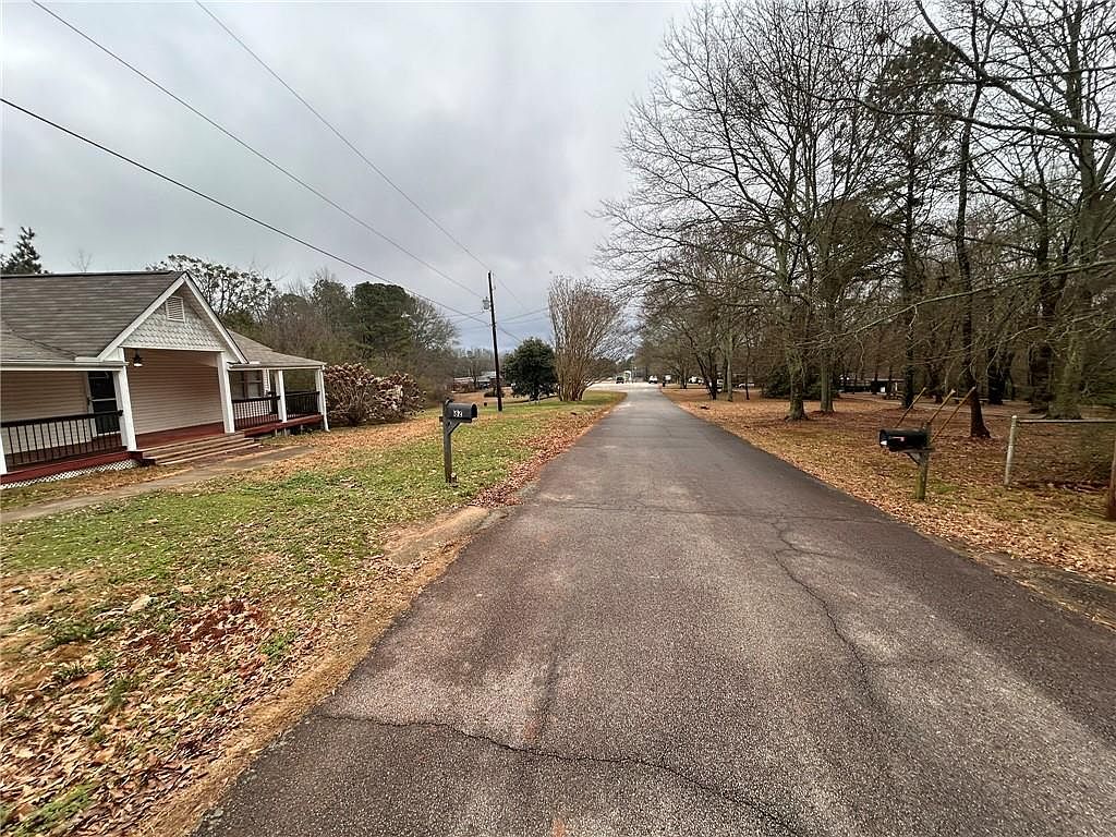 This image showcases the front view of a charming single-story house with a welcoming porch. The house is situated along a quiet street lined with mature trees, creating a peaceful and inviting atmosphere. The well-maintained lawn and the presence of a mailbox suggest a comfortable suburban setting.