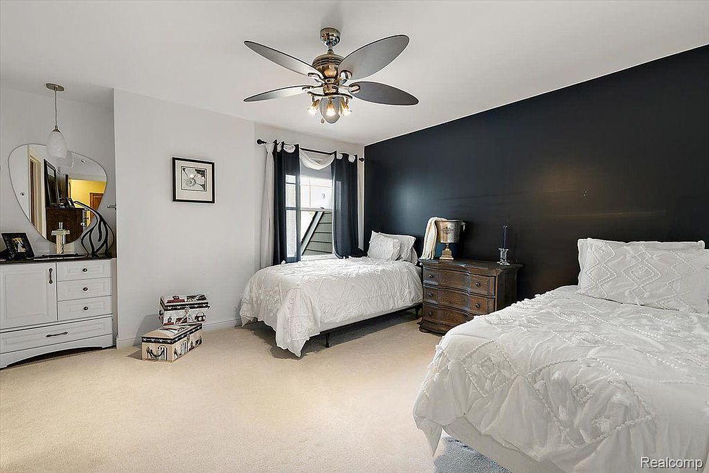 This is a guest bedroom featuring two twin beds with white bedding, a dark accent wall, and a ceiling fan. The room has a neutral carpet and includes a dresser and a small chest of drawers. The overall impression is clean and comfortable, suitable for guests.
