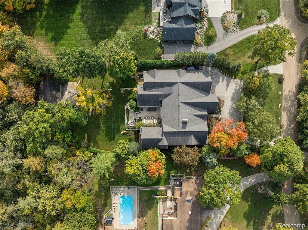 This aerial view showcases a sprawling property with a large, modern home featuring a complex roofline and well-manicured landscaping. A swimming pool and tennis court are visible, suggesting a luxurious and private estate. Mature trees and lush greenery surround the property, enhancing its appeal and seclusion.