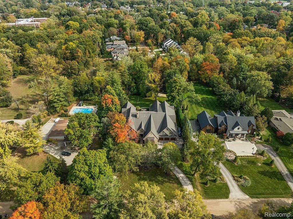 This aerial view showcases a luxurious property nestled among lush trees, highlighting the expansive grounds and multiple structures. A swimming pool is visible, adding to the estate's appeal, while the architecture suggests a blend of traditional and modern design elements. The well-maintained landscaping and mature trees create a sense of privacy and tranquility.