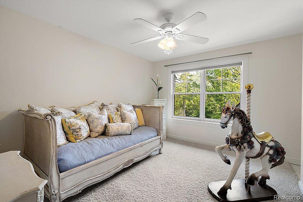 This is a charming guest bedroom featuring a daybed adorned with decorative pillows, a carousel horse statue, and a ceiling fan. The room has a cozy and inviting atmosphere, enhanced by the natural light streaming through the window. The neutral color palette and plush carpeting create a comfortable and relaxing space.
