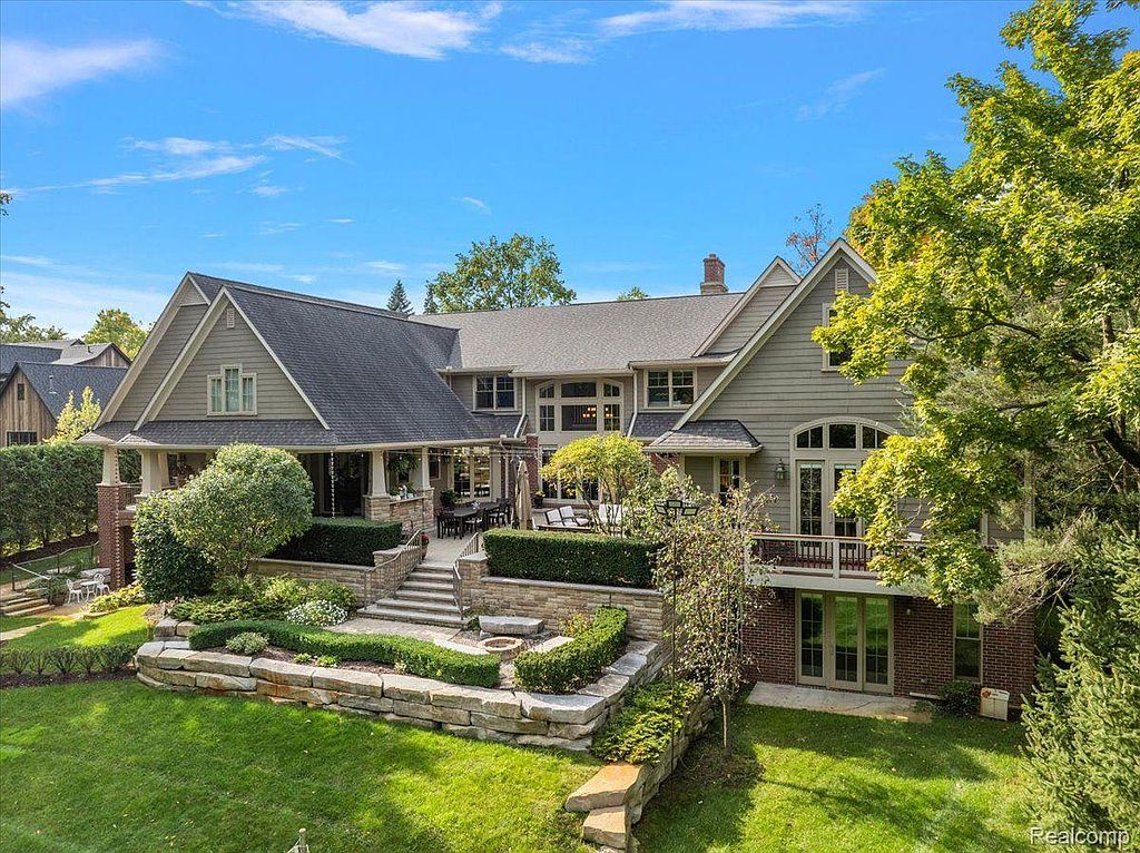 This image showcases the rear exterior of a large, well-maintained home with a multi-level backyard. The property features a spacious patio area, manicured landscaping with stone retaining walls, and a walk-out basement. The architectural style is traditional with a modern touch, emphasizing outdoor living and entertainment.