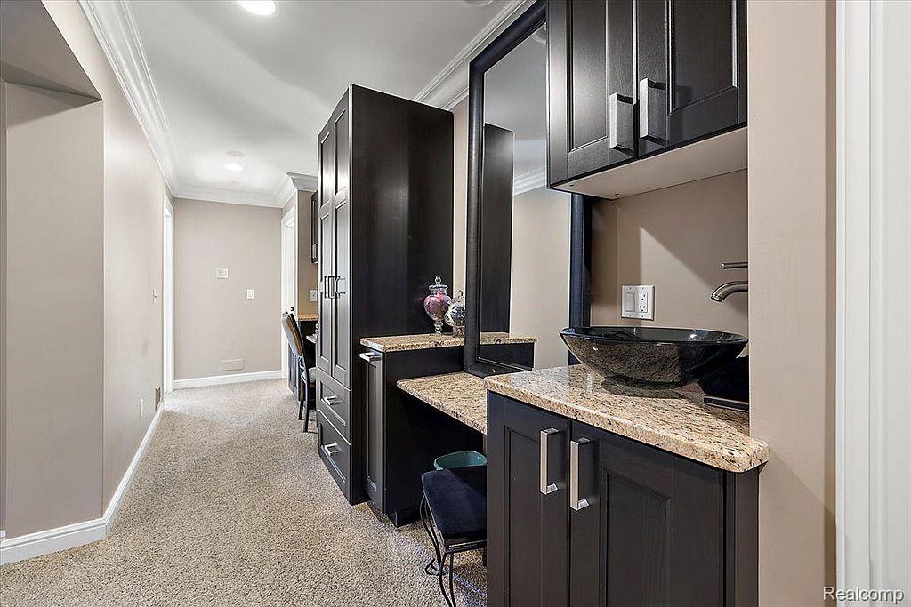 This image showcases a stylish bathroom vanity area with dark cabinetry, granite countertops, and a vessel sink. A large mirror and ample storage space enhance the functionality of the area. The neutral wall color and carpet create a warm and inviting atmosphere.