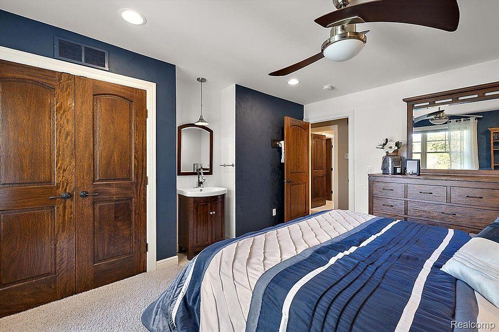 This primary bedroom features a blue and white striped bed, dark wood dresser with a mirror, and a small vanity area. The walls are painted in a combination of white and navy blue, creating a cozy and inviting atmosphere. The room is well-lit with recessed lighting and a ceiling fan.