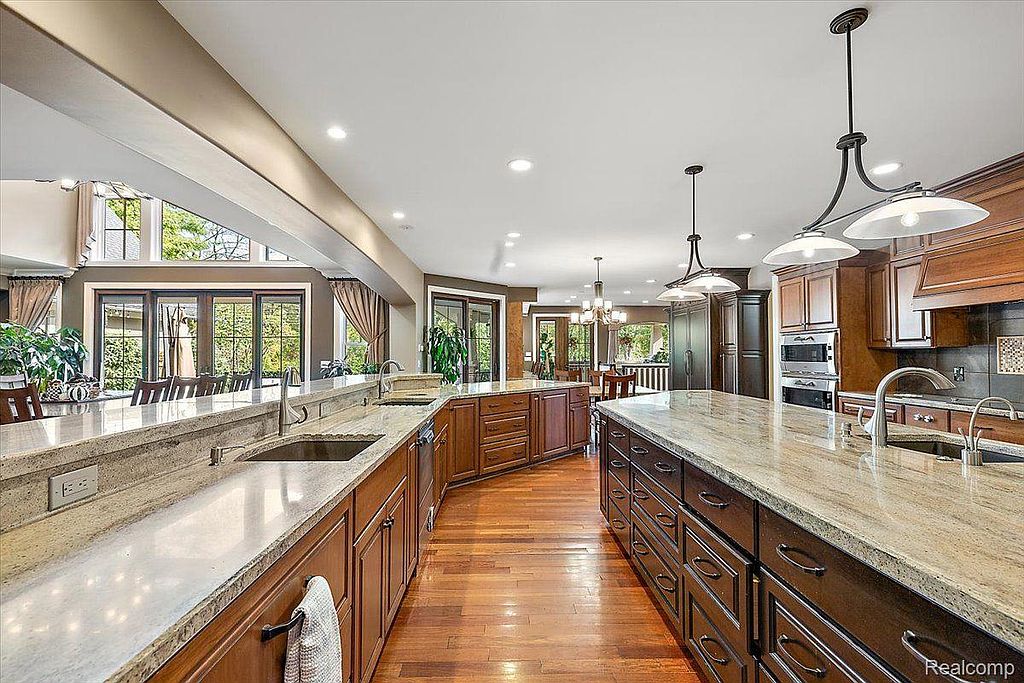 This is a spacious kitchen featuring wooden cabinetry, granite countertops, and hardwood floors. The kitchen includes a large island with a sink and ample storage, as well as modern appliances. Large windows provide natural light and views of the outdoors, creating a warm and inviting atmosphere.
