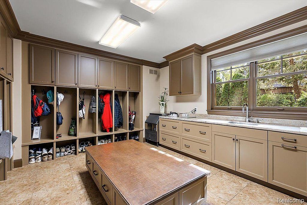 This is a well-organized laundry room featuring custom built-in storage with individual cubbies and upper cabinets. A large central island provides ample workspace, and a window offers natural light. The neutral color palette and clean design create a functional and aesthetically pleasing space.