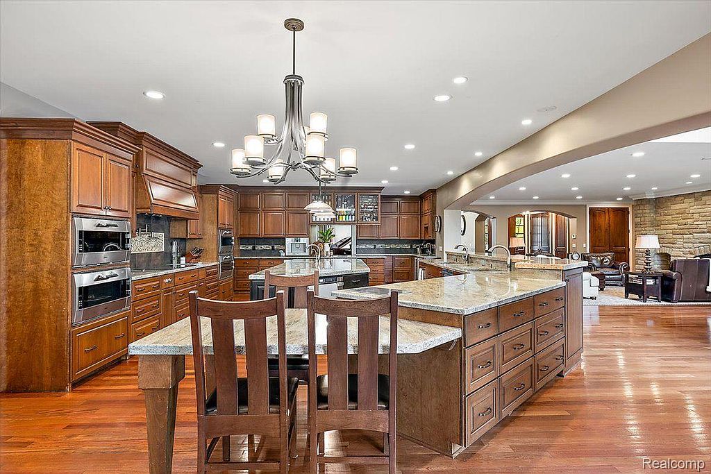 This is a spacious kitchen featuring dark wood cabinetry, granite countertops, and stainless steel appliances. A large island with seating provides ample workspace, and a chandelier adds a touch of elegance. The hardwood floors and open layout create a warm and inviting atmosphere.