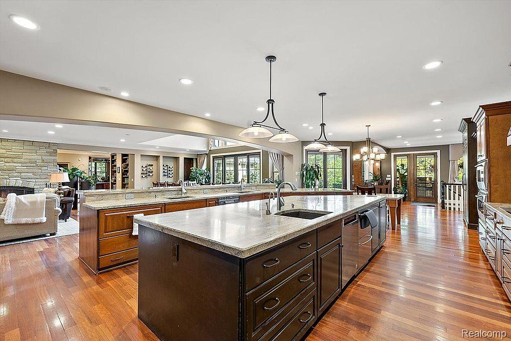 This is a spacious kitchen featuring hardwood floors, a large island with a sink, and granite countertops. The kitchen has dark wood cabinetry and stainless steel appliances. The open layout connects to other living spaces, creating a welcoming and functional area.