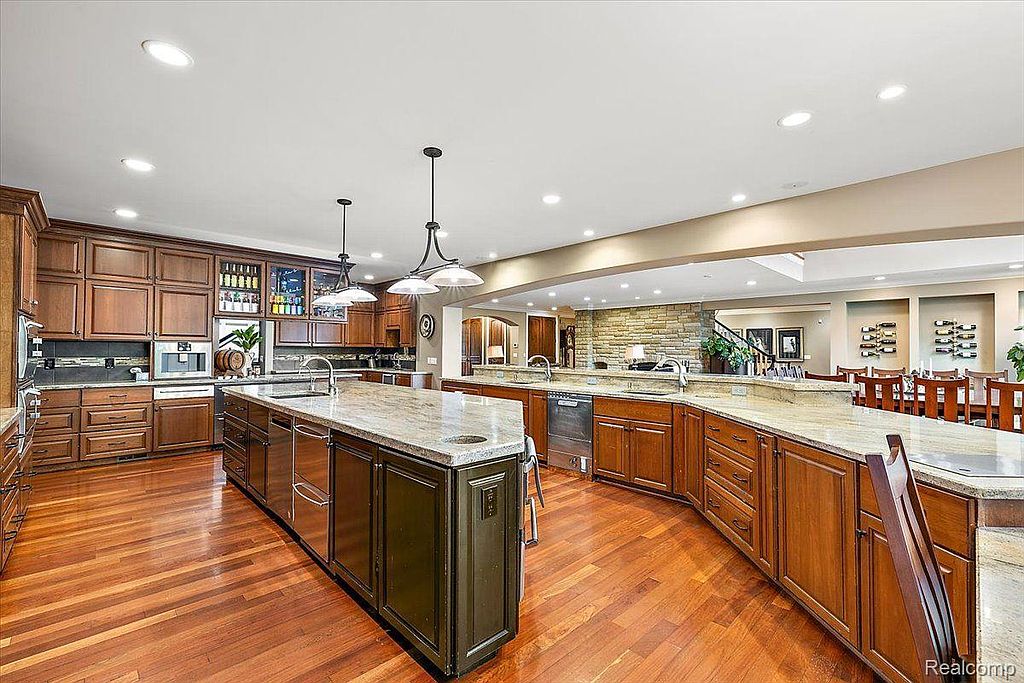This is a spacious kitchen featuring dark wood cabinetry, granite countertops, and stainless steel appliances. A large island provides ample workspace, and pendant lighting illuminates the area. The hardwood floors add warmth to the space, creating a luxurious and inviting atmosphere.