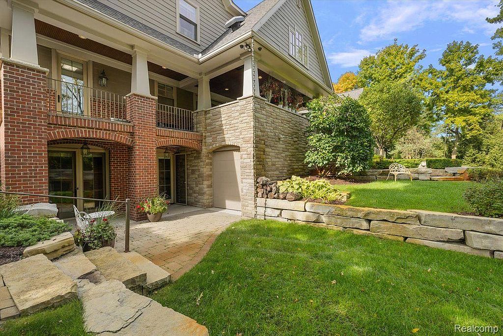 This image showcases a beautifully landscaped yard with a stone retaining wall, lush green grass, and mature trees. The architecture of the house is visible in the background, featuring a combination of brick and stone elements. The overall impression is one of a well-maintained and inviting outdoor space.
