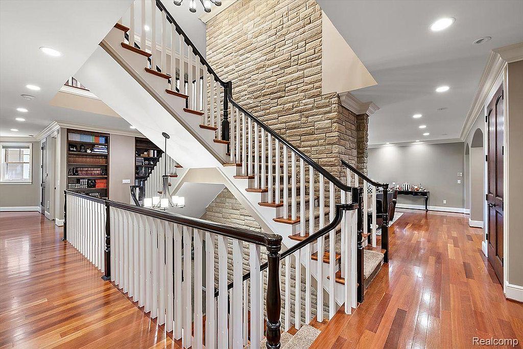 This interior shot showcases a grand hallway and staircase. The staircase features a combination of wood and white balusters, complemented by a stone accent wall. The hardwood flooring adds warmth and elegance to the space, creating a luxurious and inviting atmosphere.