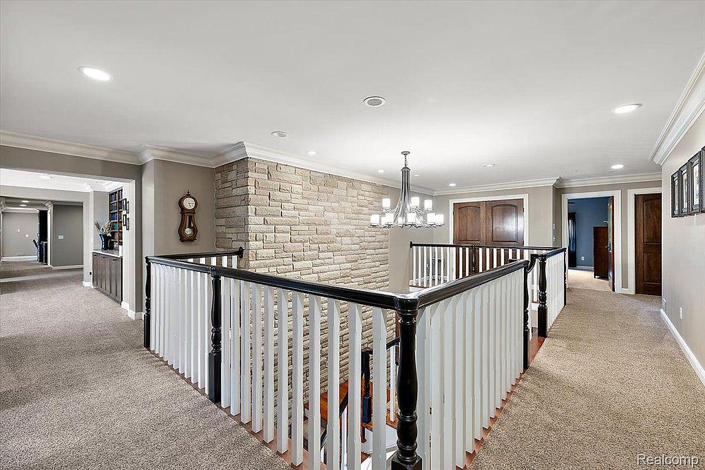 This interior shot showcases a well-lit hallway with a staircase. The hallway features neutral-toned carpet, a decorative stone wall, and a railing with white balusters and a dark wood handrail. The space is clean and appears spacious, suggesting a well-maintained home.