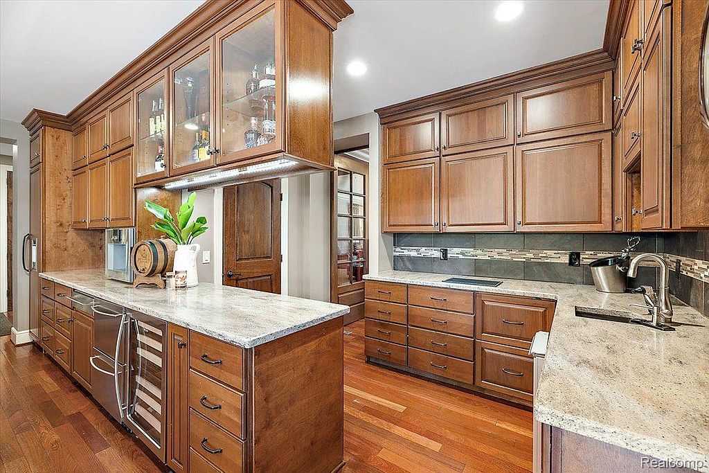 This is a well-appointed kitchen featuring custom wood cabinetry, granite countertops, and stainless steel appliances. The kitchen includes a wine refrigerator and a built-in bar area with glass-front cabinets. The hardwood flooring adds warmth and elegance to the space.