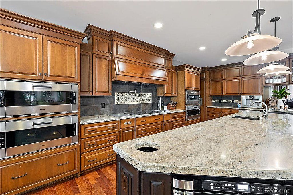This is a well-appointed kitchen featuring custom wood cabinetry, granite countertops, and stainless steel appliances, including double ovens. The large island provides ample workspace, and the overall design exudes a sense of warmth and luxury. The hardwood flooring adds to the kitchen's sophisticated appeal.
