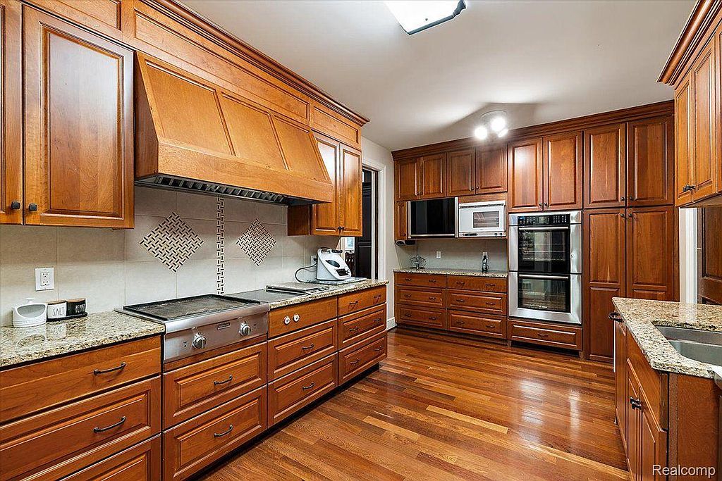 This is a well-appointed kitchen featuring rich wood cabinetry, granite countertops, and stainless steel appliances. The layout includes ample storage and counter space, with a built-in oven and microwave. The hardwood flooring adds warmth and elegance to the space.