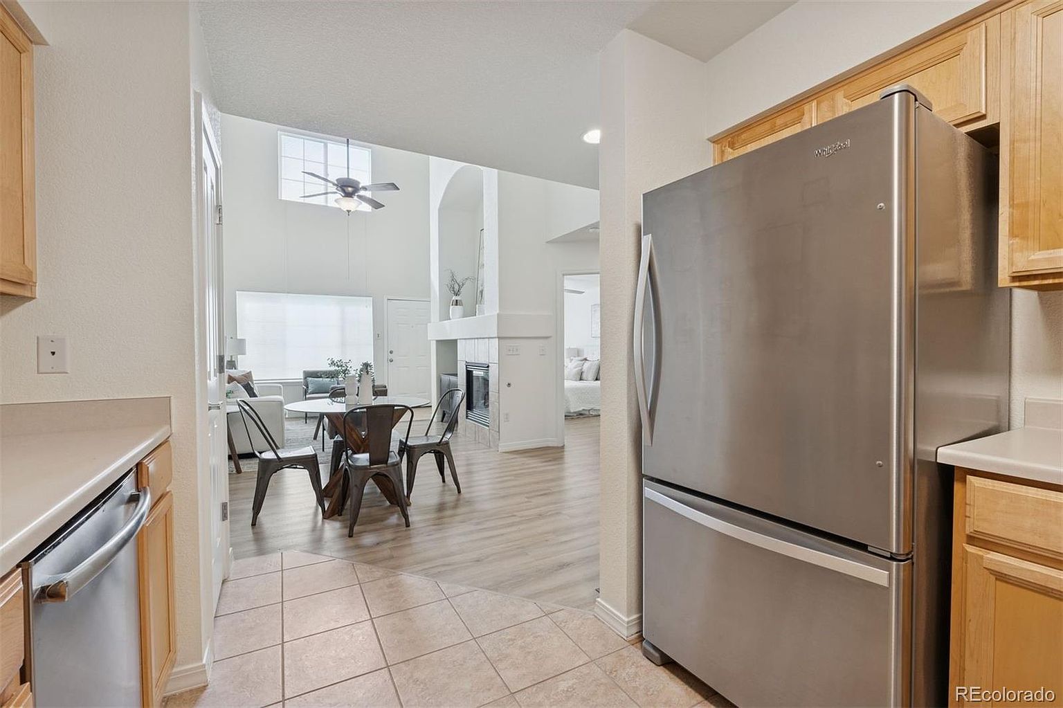 This interior shot showcases a kitchen that flows seamlessly into the dining and living areas. The kitchen features light wood cabinetry and stainless steel appliances, including a prominent refrigerator. The open layout allows for easy interaction between the kitchen and the adjacent spaces, creating a welcoming and connected living environment.