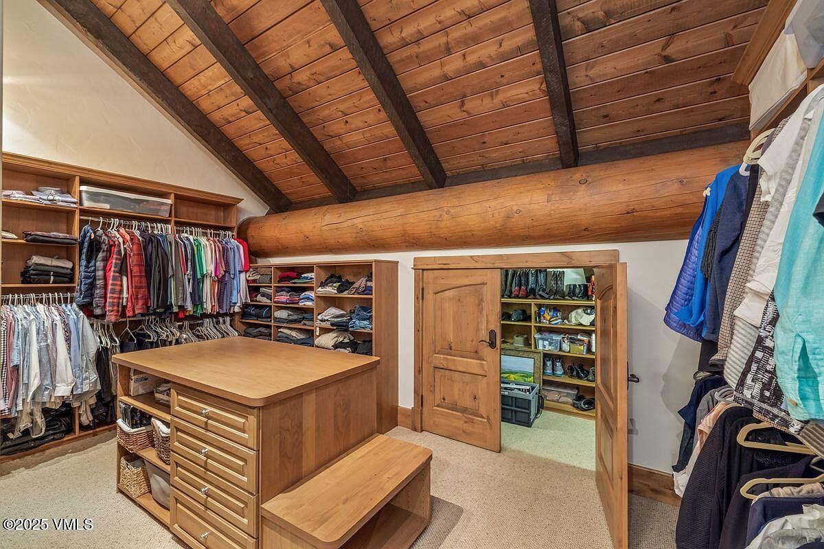 This is a well-organized walk-in closet featuring custom wooden shelving and drawers. Clothes are neatly hung and folded, and a central island provides additional storage and a surface for organizing. The closet also includes a separate shoe storage area, showcasing a luxurious and functional design.